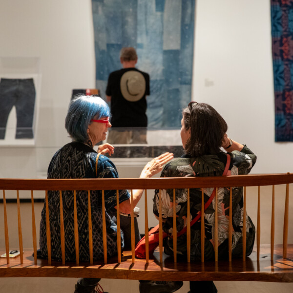 Two women sitting on a bench inside the Blue Gold exhibition at Mingei