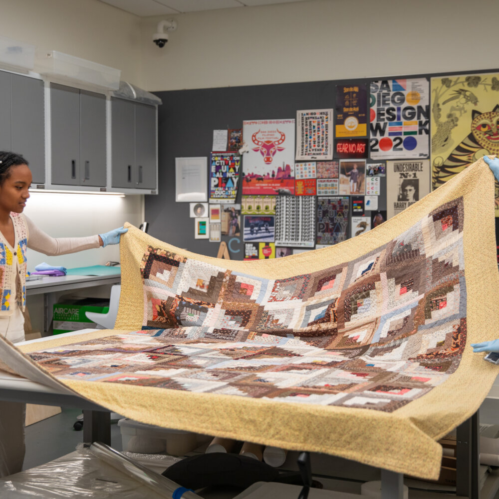 Olivia and Guusje unfolding a quilt in the collections space