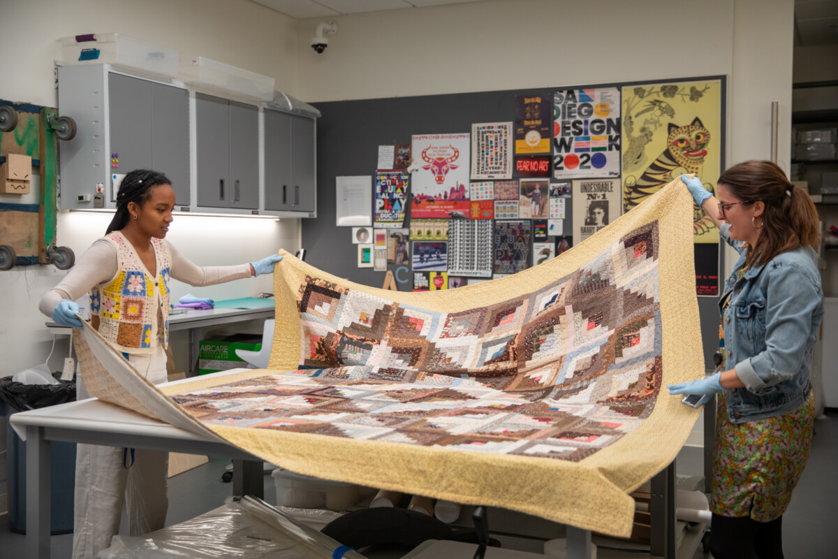 Olivia and Guusje unfolding a quilt in the collections space