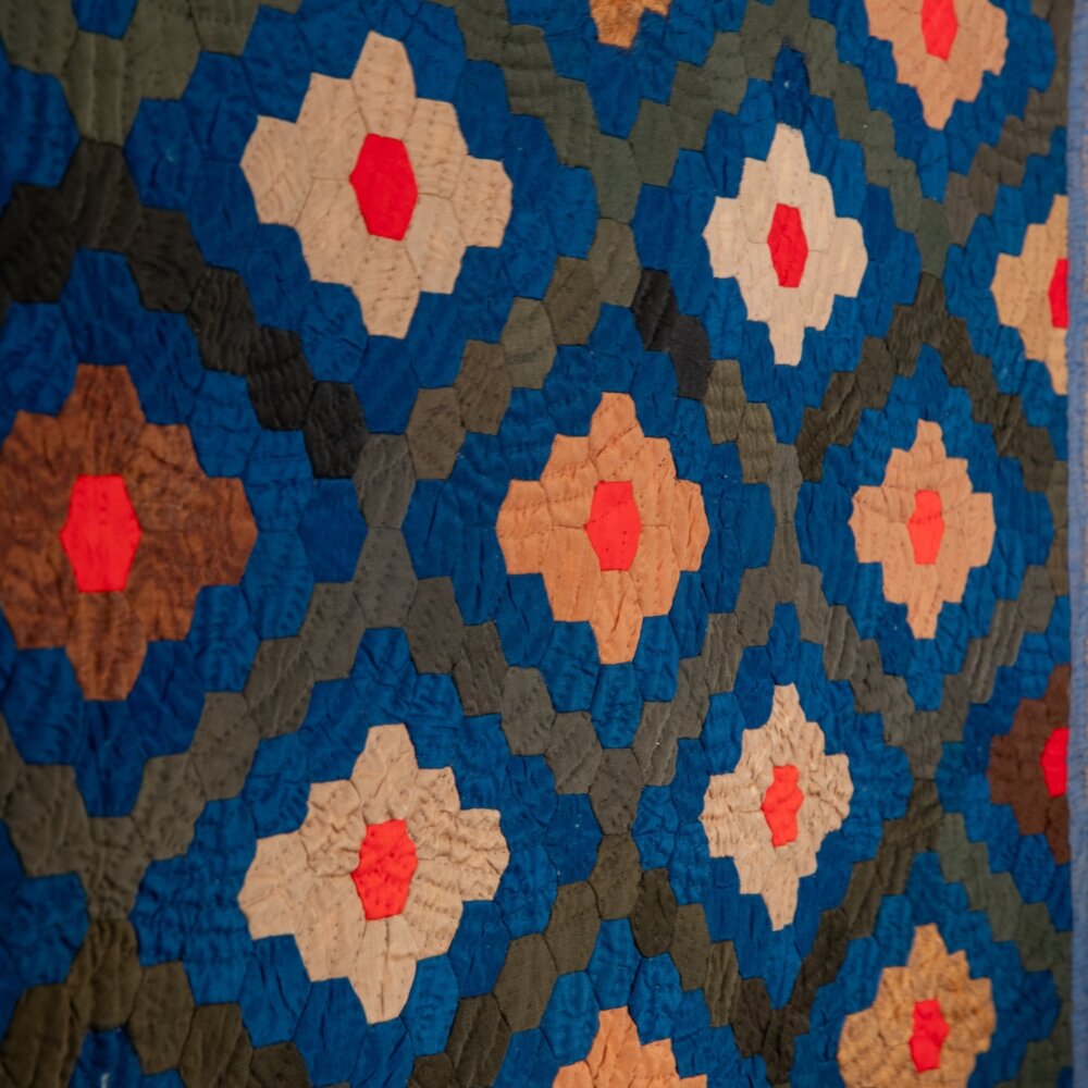 Quilt with diamond pattern made of grey, blue, tan, brown, and red hexagons