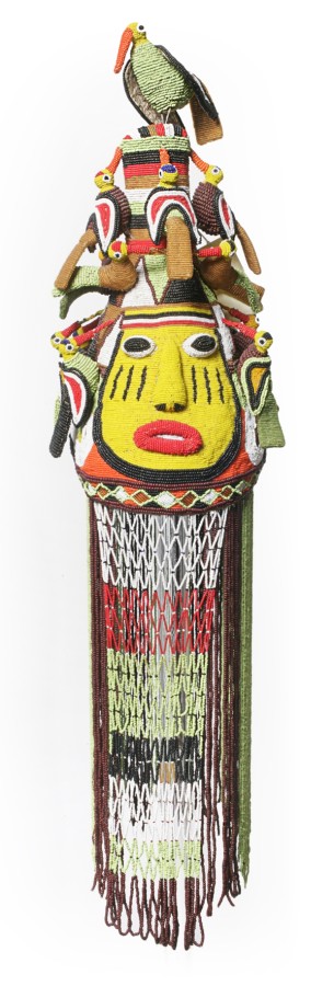 This crown is beaded from top to bottom. On top of the crown sits a bead bird and below the bird is a human face. Long strands of beads are below the face.