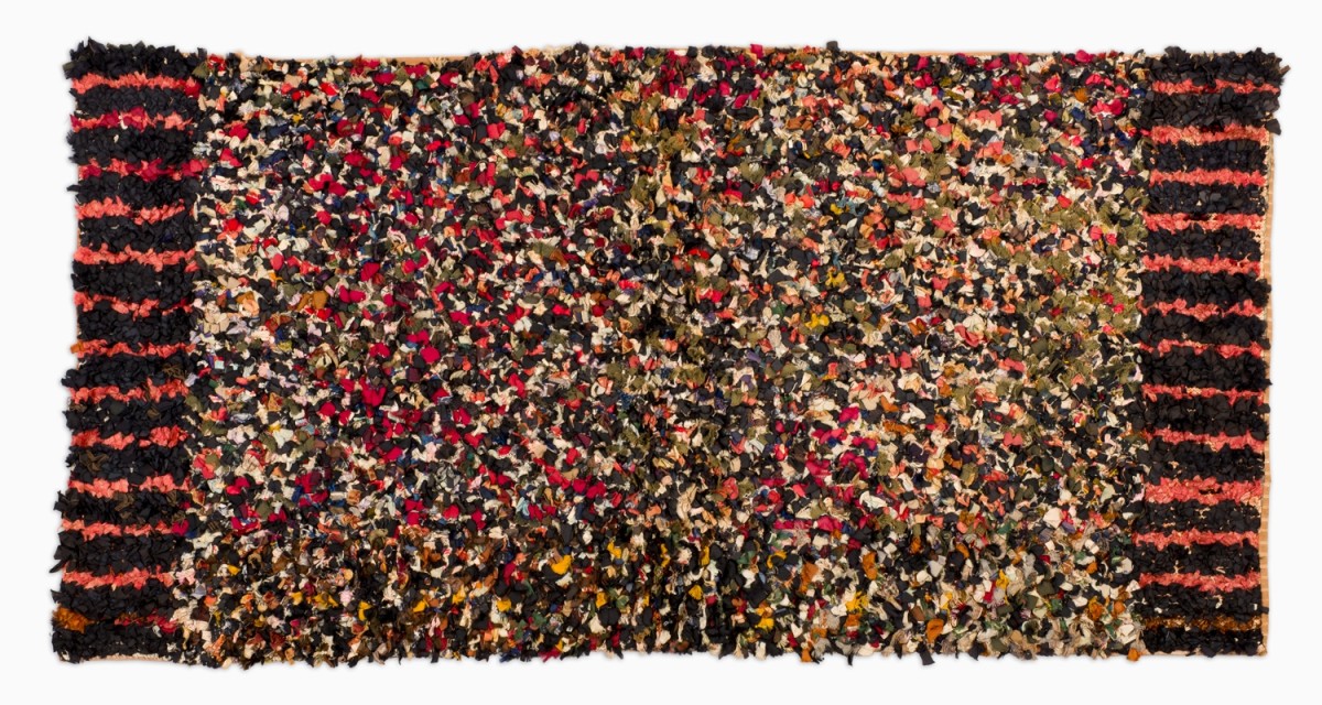 Thousands of strips of silk and velvet fabric were individually hand-tied to a knitted cotton base to create this rag rug. Two sides, opposite each other are orange and black striped and the center is a multitude of colors.