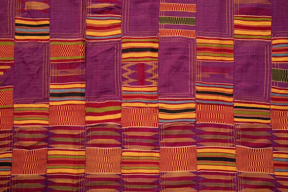 Detail of textile with a purple base fabric decorated with geometric with shapes and designs in yellow, blue, red, black, and green.