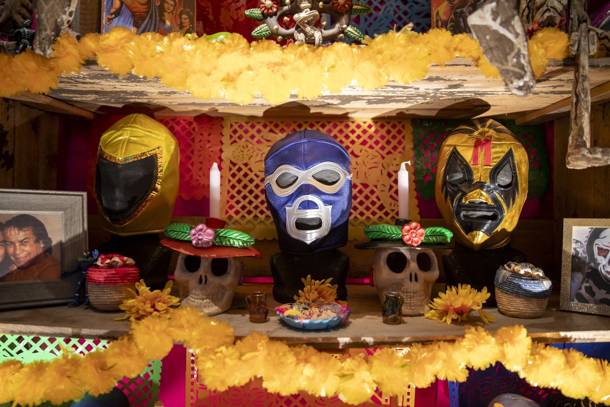 Dia de los Muertos altar with luchadores masks, photos, skulls, and decorations.