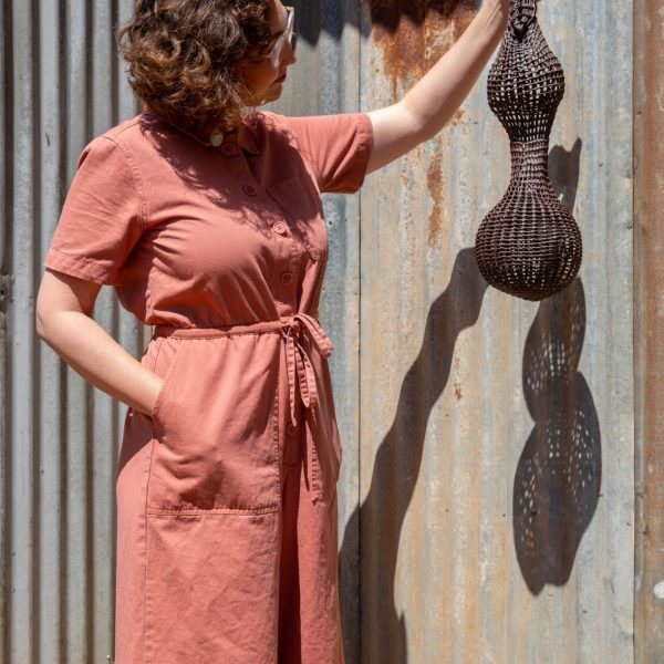 Cara Golden holds mesh sculpture piece up against a rusty steel wall.
